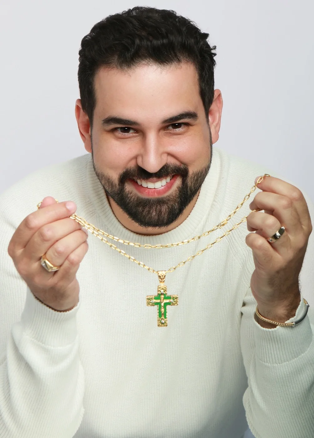 Retrato de Danillo sorrindo e segurando um colar de cruz com pedras verdes